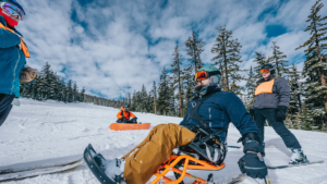 Image of skiiers and snowboarders using accessible equipment in a snowy skihill