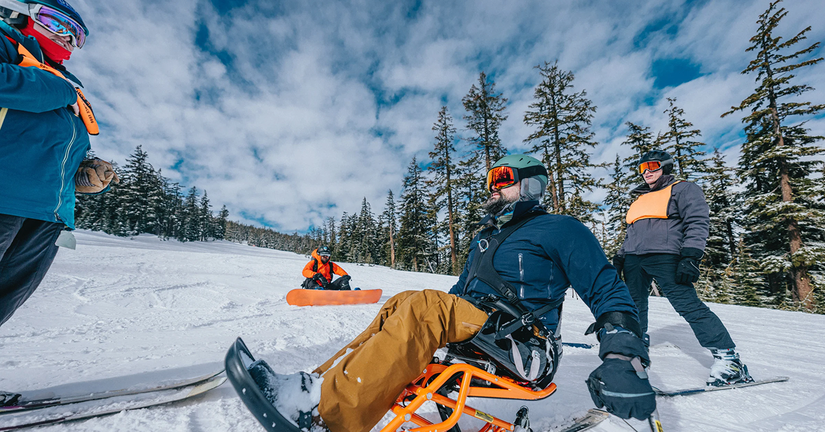 Image of skiiers and snowboarders using accessible equipment in a snowy skihill